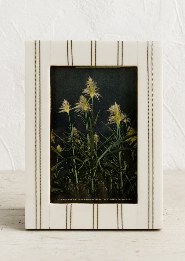An ivory resin picture frame with vertical brass ticking stripe detail.