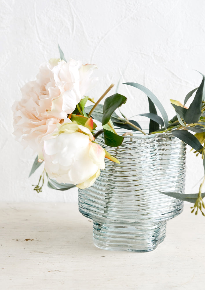 A ribbed blue glass vase with peonies.