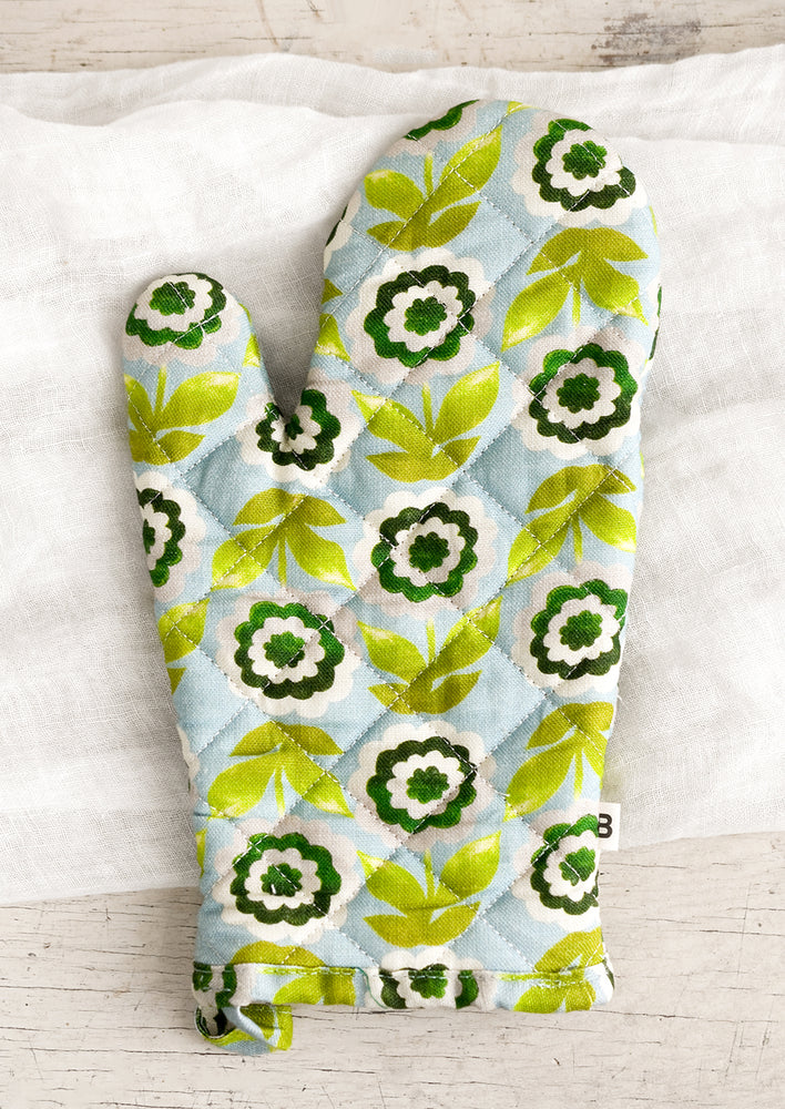 A quilted oven mitt in blue with green flowers.