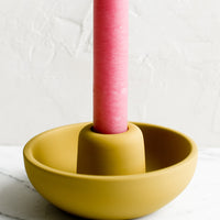 Mustard: A matte taper candle holder with bowl-like base in mustard with pink candle.