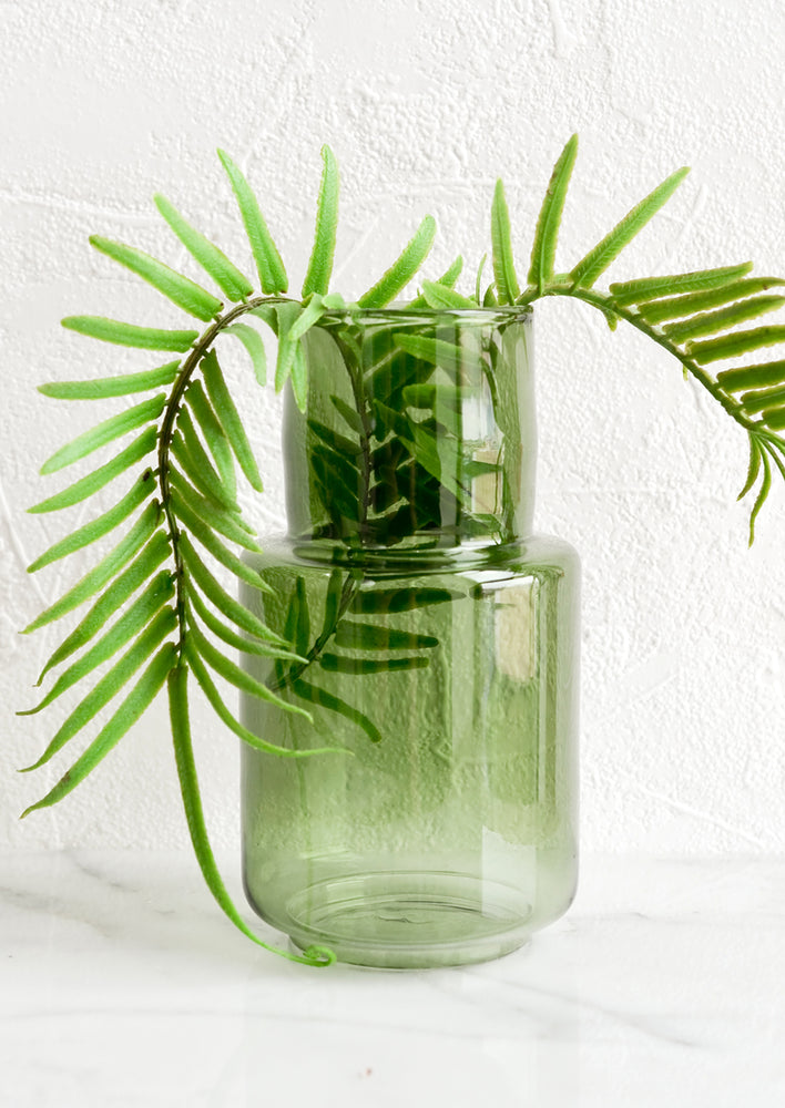 A green glass vase with fern.