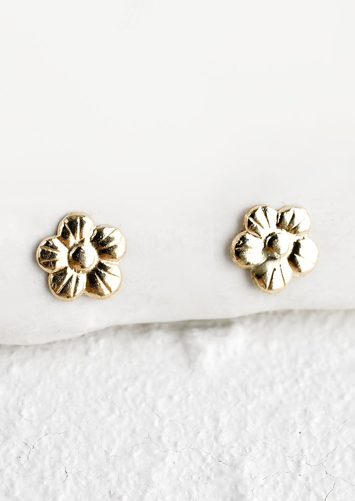 A pair of tiny gold flower stud earrings.
