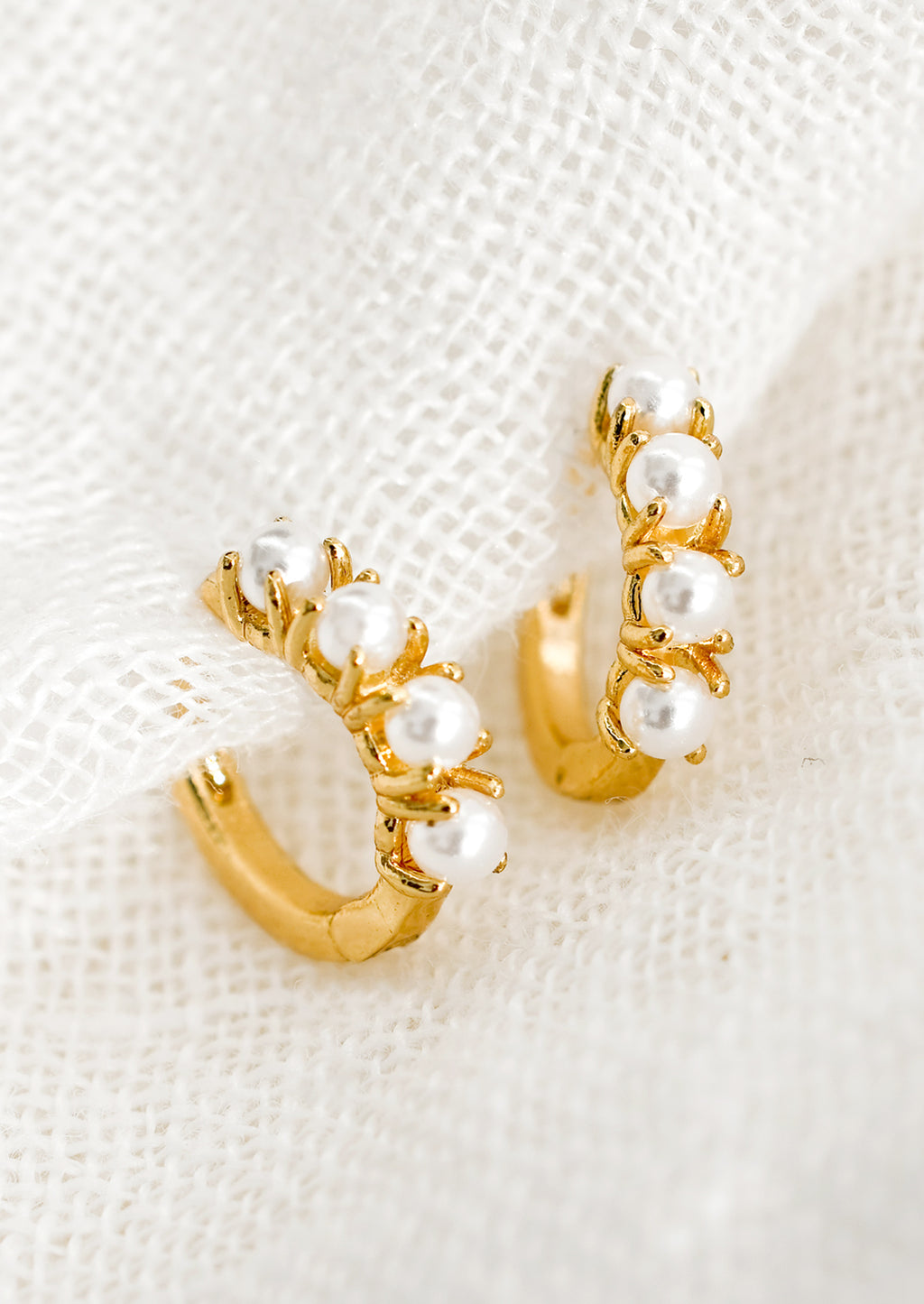 1: A pair of small gold huggie hoop earrings with round pearl detailing.