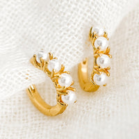 1: A pair of small gold huggie hoop earrings with round pearl detailing.