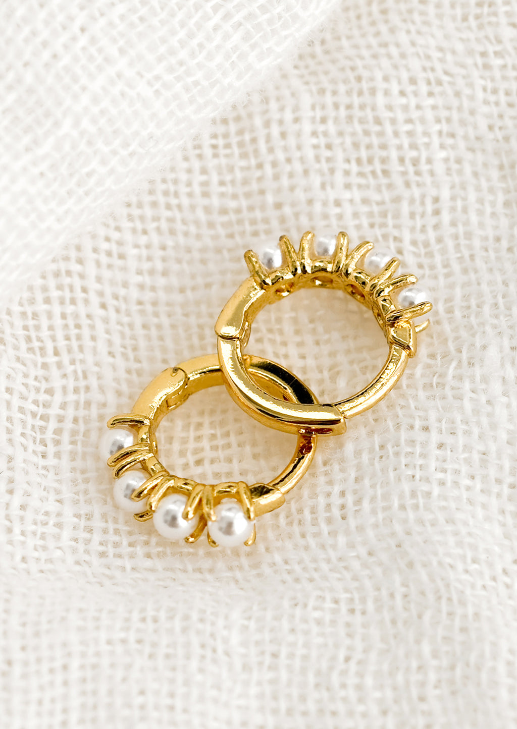 2: A pair of small gold huggie hoop earrings with round pearl detailing.