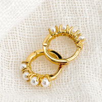 2: A pair of small gold huggie hoop earrings with round pearl detailing.