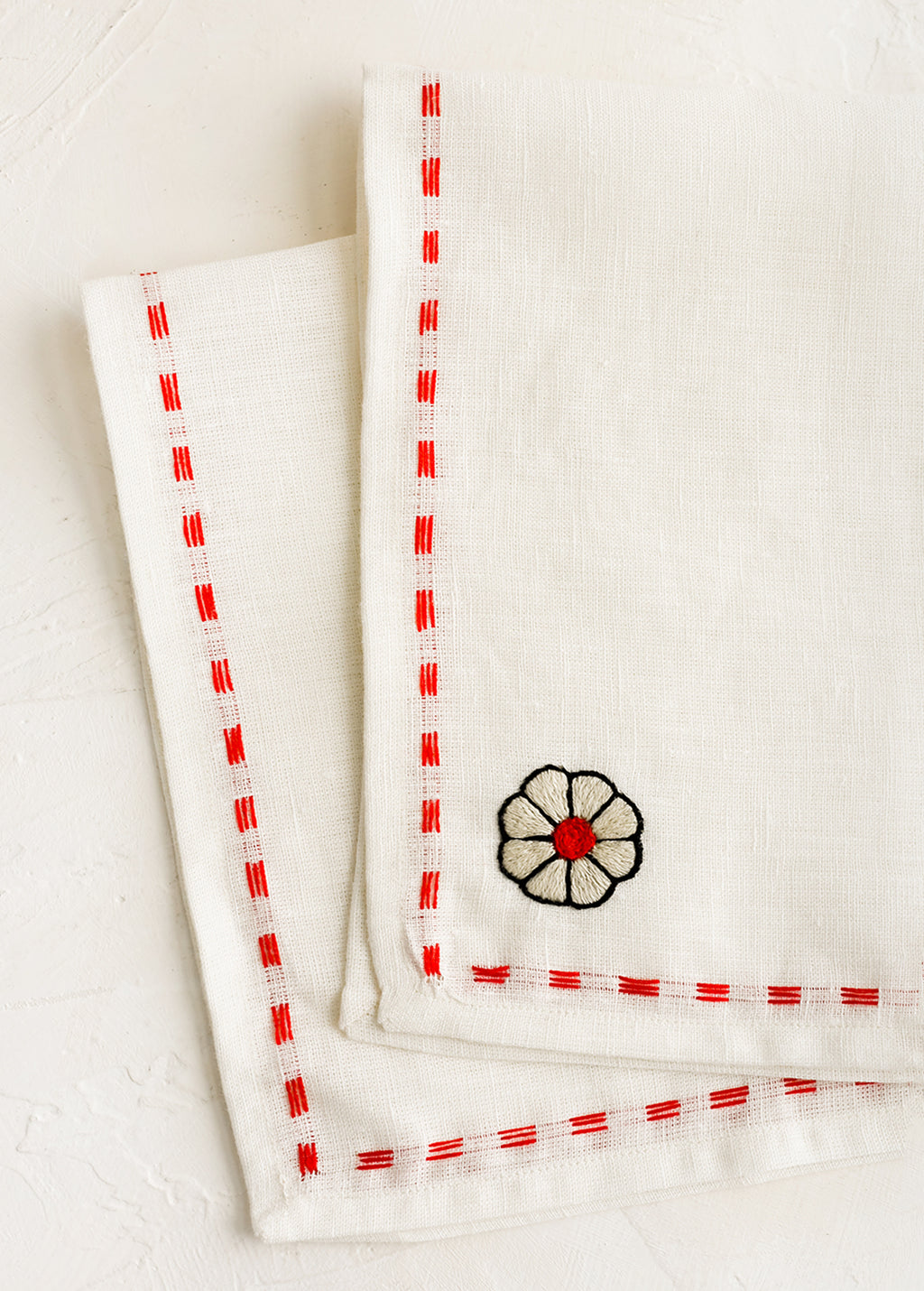 2: A white linen napkin with embroidery detailing in red.