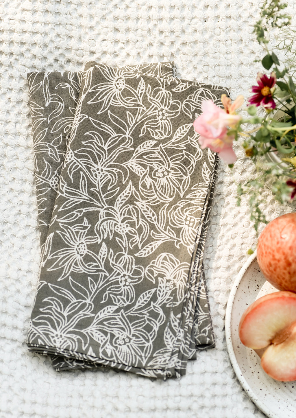 1: A pair of grey and white floral print napkins on blanket.