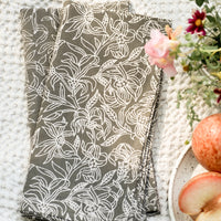 1: A pair of grey and white floral print napkins on blanket.
