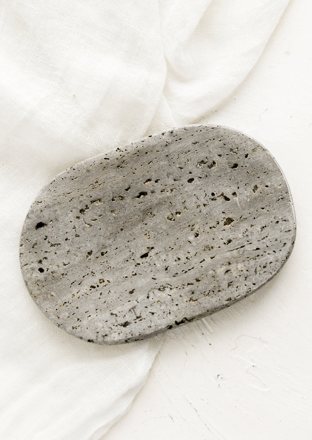 1: An oval-shaped soap dish in grey travertine.