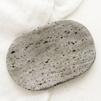 1: An oval-shaped soap dish in grey travertine.