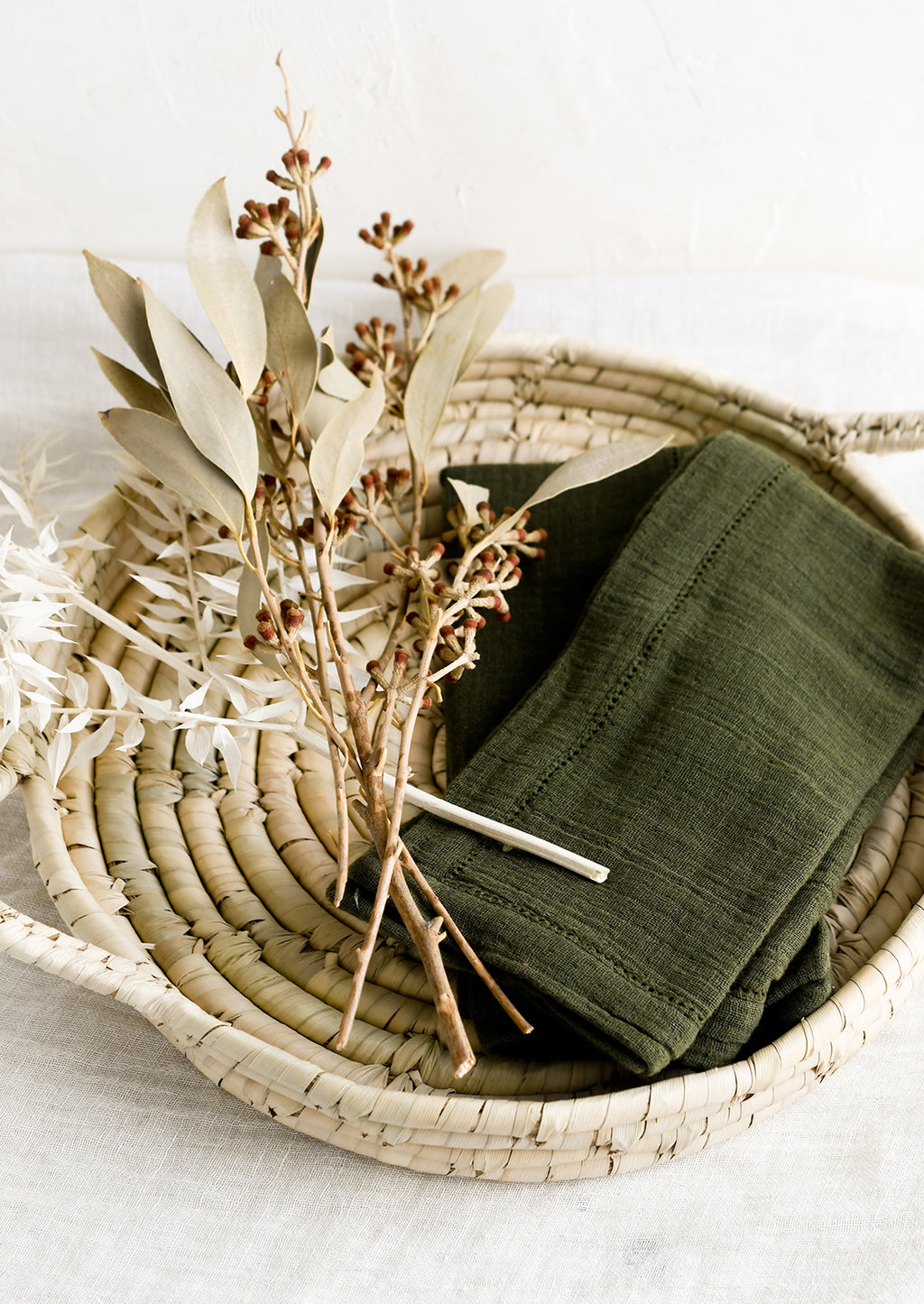 3: A round woven tray holding dried flowers and napkins.