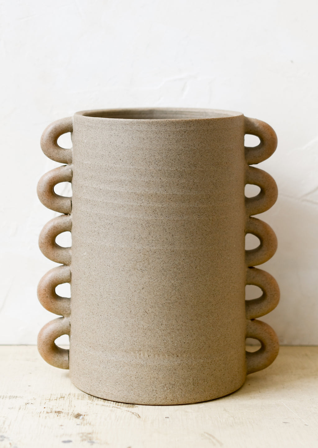 1: A raw sand clay vase with decorative loops all the way down both sizes.