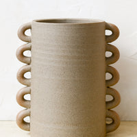 1: A raw sand clay vase with decorative loops all the way down both sizes.