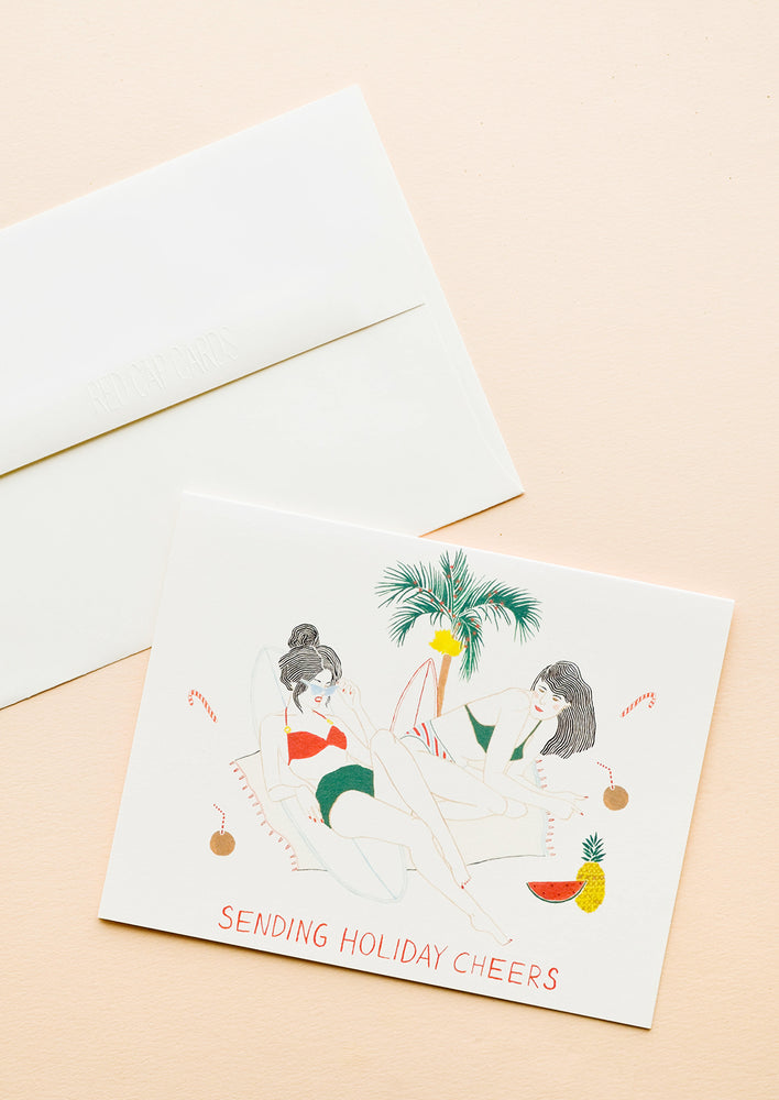 1: Greeting card with two women lounging below palm tree with tropical drinks and candy canes, text reads "Sending holiday cheers"