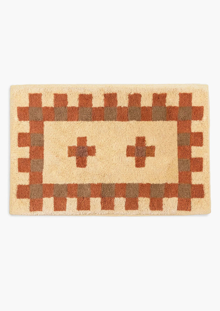 A bath mat in geometric cross print in peach, terracotta and brown.