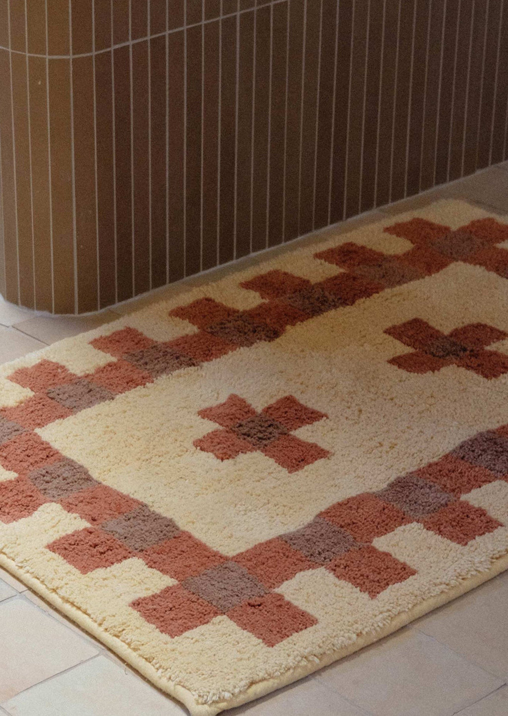 2: A bath mat in geometric cross print in peach, terracotta and brown.