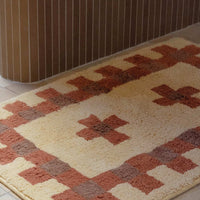 2: A bath mat in geometric cross print in peach, terracotta and brown.