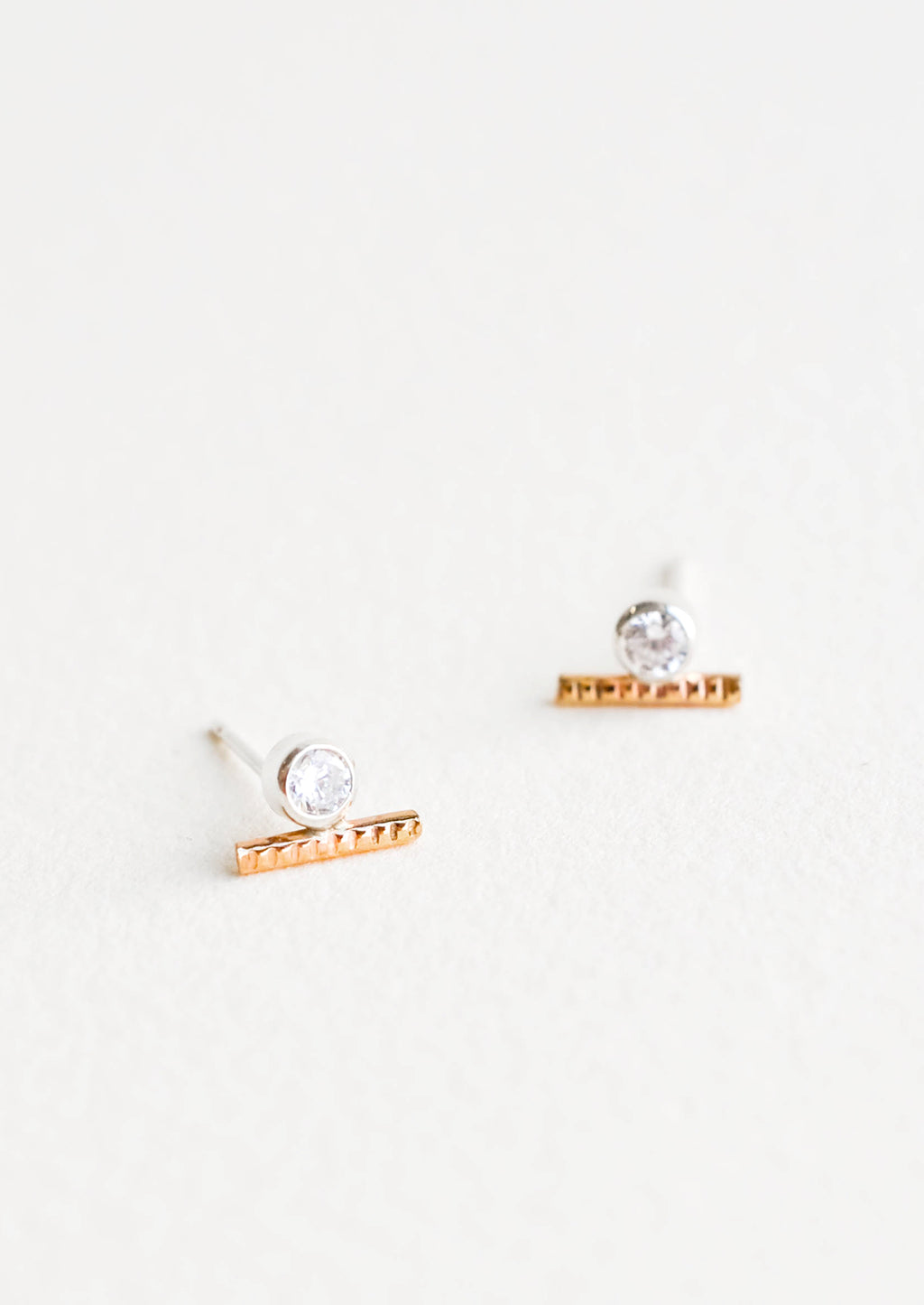 1: Stud earrings with a round white crystal set in a silver, attached to a short textured gold bar.