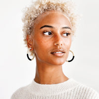 2: Model wears black and white beaded hoop earrings and white sweater.