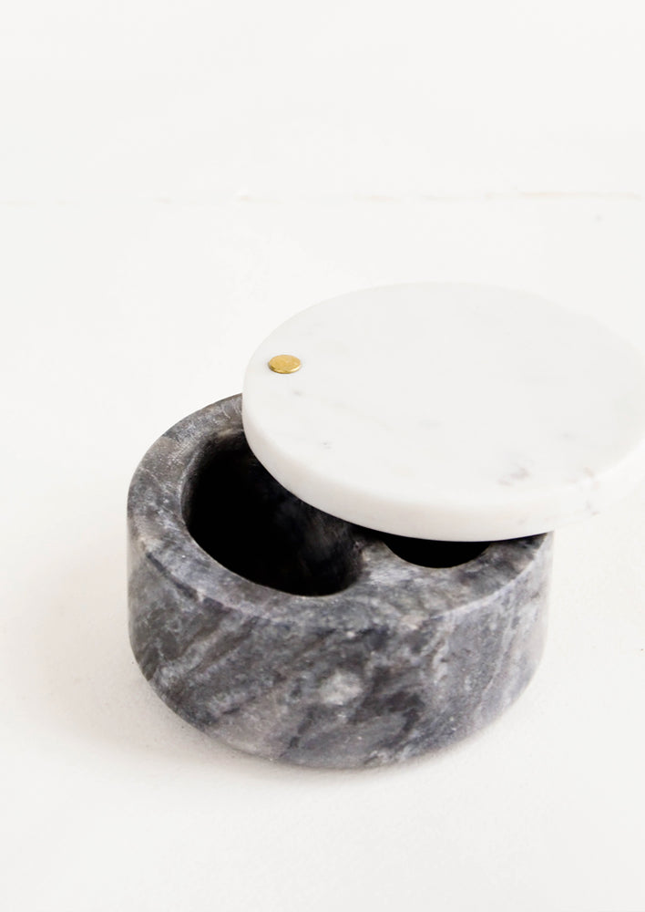 Round salt cellar made of black marble with pivoting white marble lid