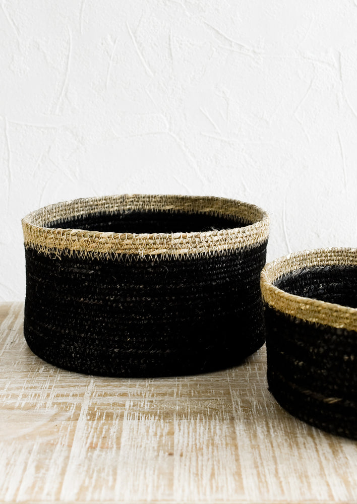 A shallow circular basket in black with tan rim, in small and medium sizes.