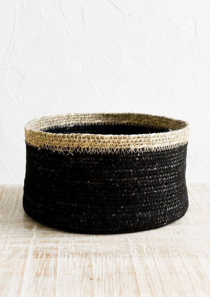 A shallow circular basket in black with tan rim.