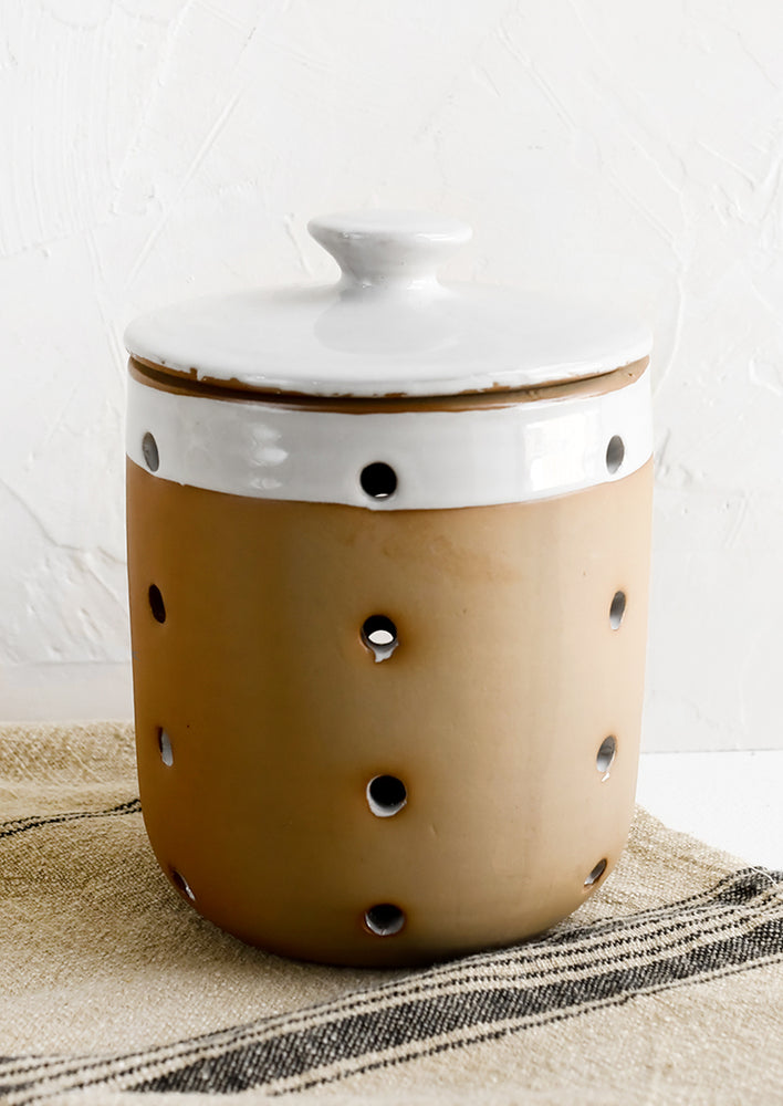 A ceramic lidded jar with white glaze dip detailing and brown body.