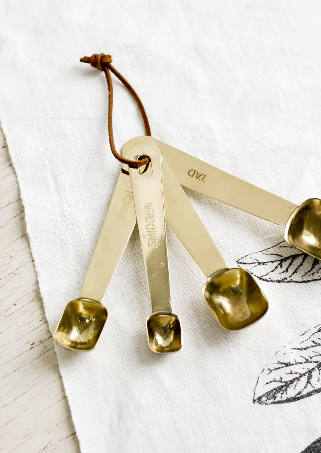 1: A set of four golden measuring spoons with brown leather tie.