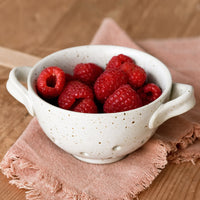 1: A small ceramic colander holding raspberries.
