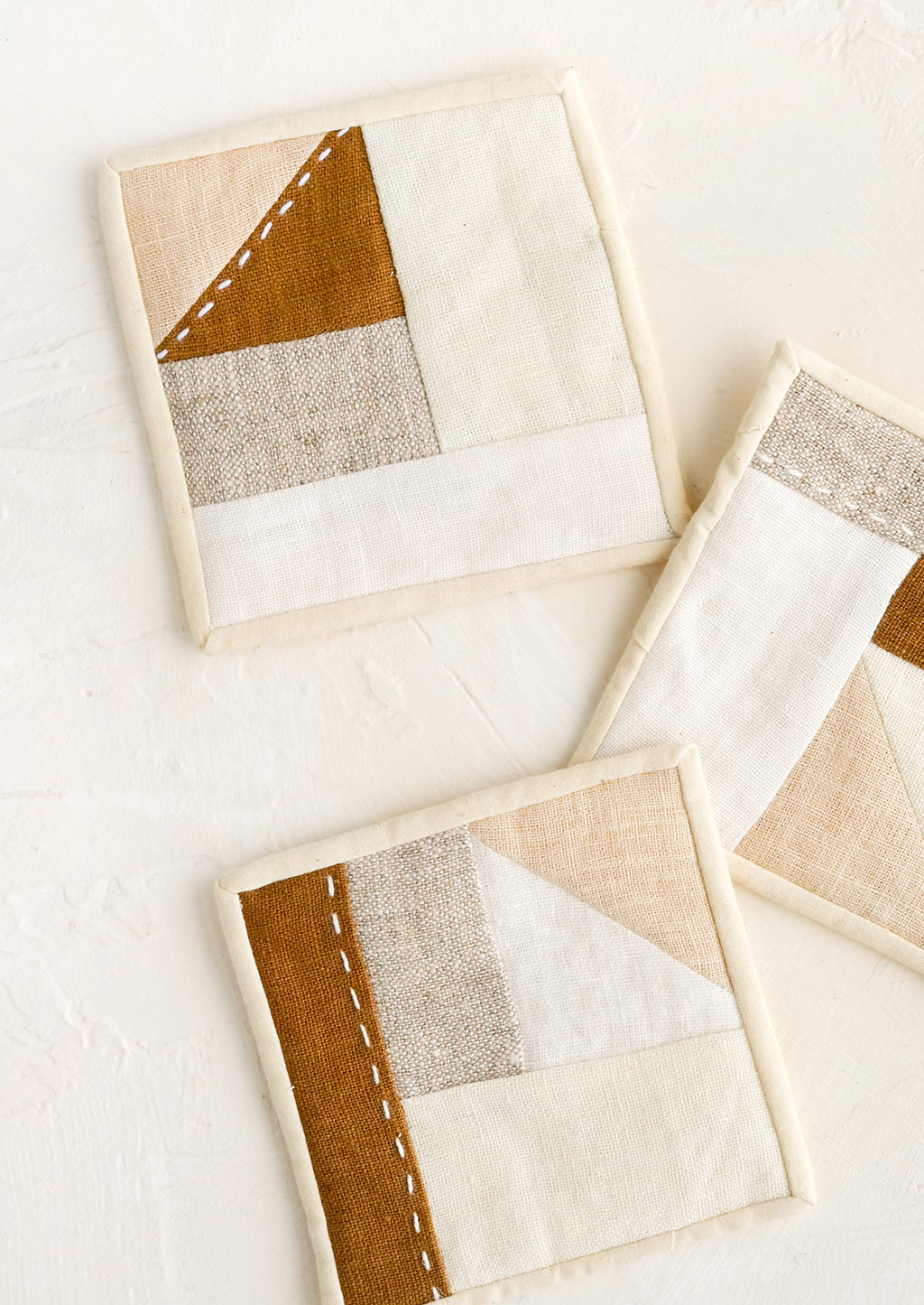 1: Three square drink coasters made from neutral hued patchwork fabric.