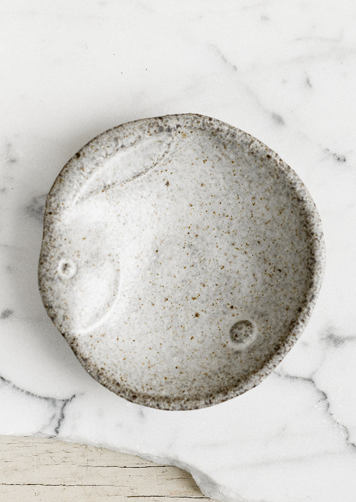 A round ceramic dish in speckled grey glaze with rabbit design.