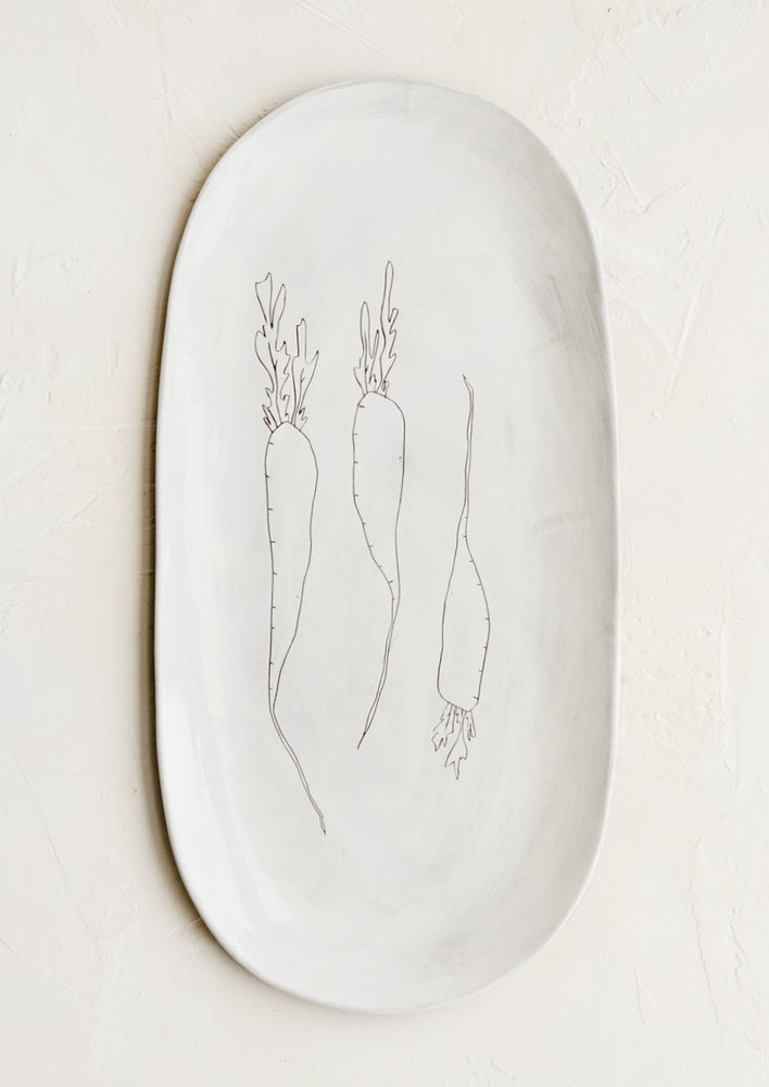 An oval shaped ceramic serving platter with hand drawn carrots illustration at center.