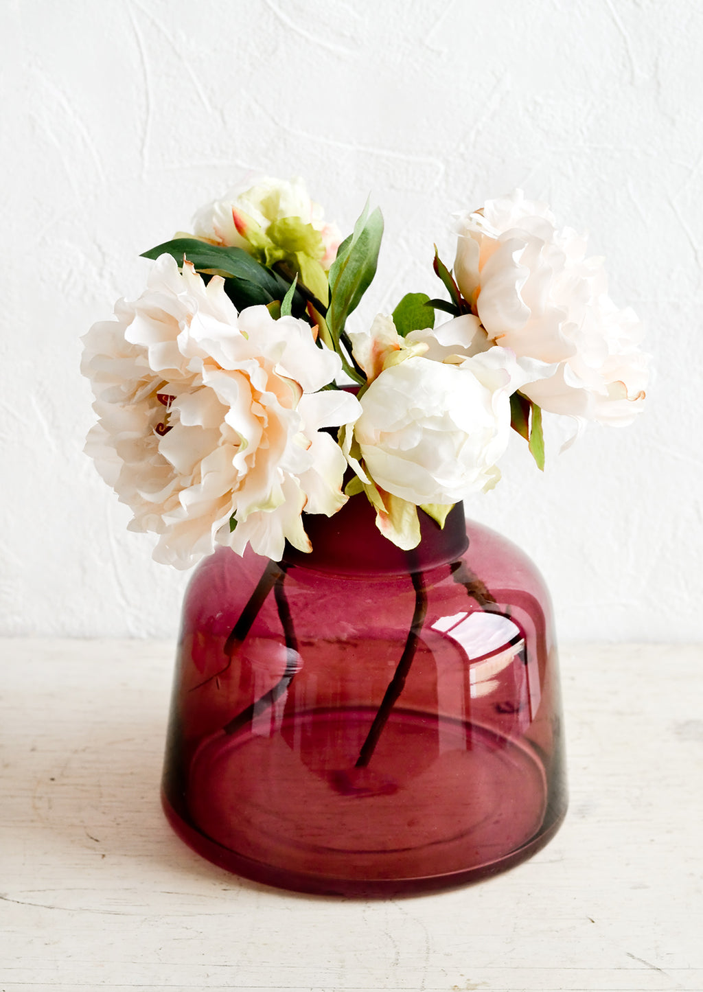 1: A berry colored glass vase with peonies.