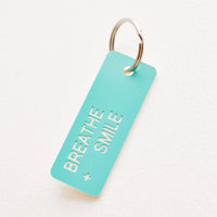Breathe + Smile: Small acrylic keychain, turquoise background with white words that says "BREATHE + SMILE"