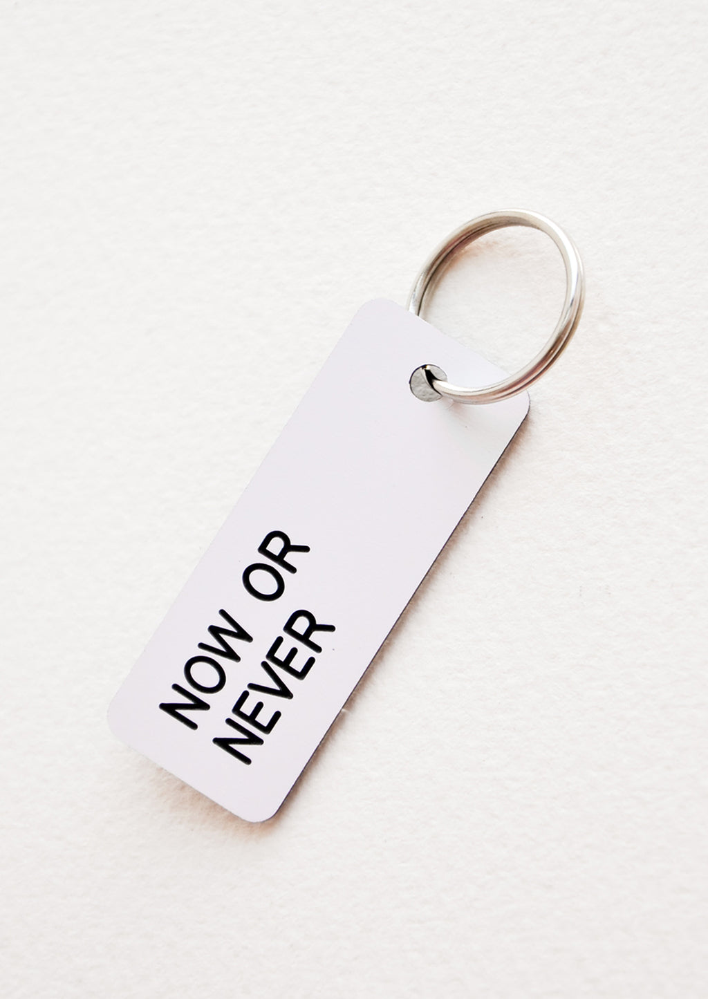 Now or Never: Small acrylic keychain, white background with black words that says "NOW OR NEVER"