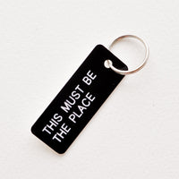 This Must Be The Place: Small acrylic keychain, black background with white words that says "THIS MUST BE THE PLACE"