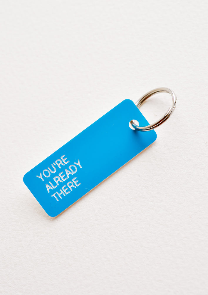 Small acrylic keychain, blue background with white words that says "YOU'RE ALREADY THERE"