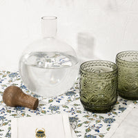 3: A glass decanter and cups pictured with scarab napkins.