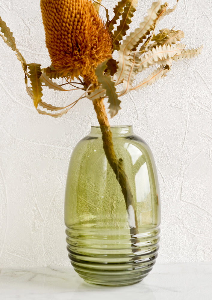 2: A ribbed green glass vase holding a dried protea flower.