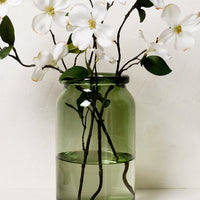 1: A tall green glass vase with dogwood branches.