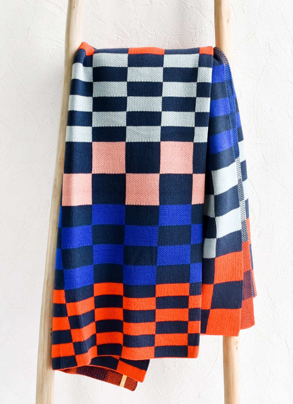 1: A knit throw blanket in checker print pattern in navy, light blue, royal blue, pink and orange.