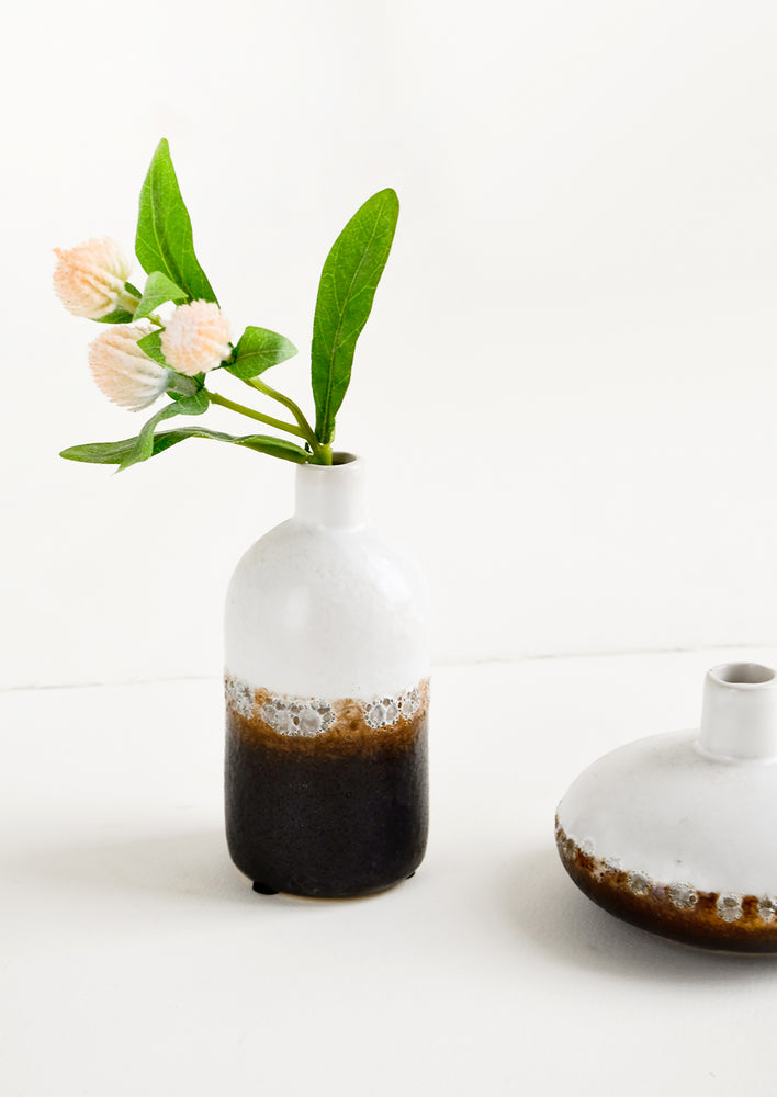 A ceramic bud vase in white and brown distressed glaze with a gomphrena stem.
