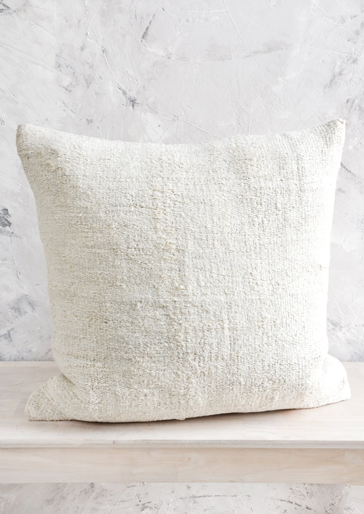 Throw pillow made from ivory colored vintage hemp fabric, sitting on a bench.