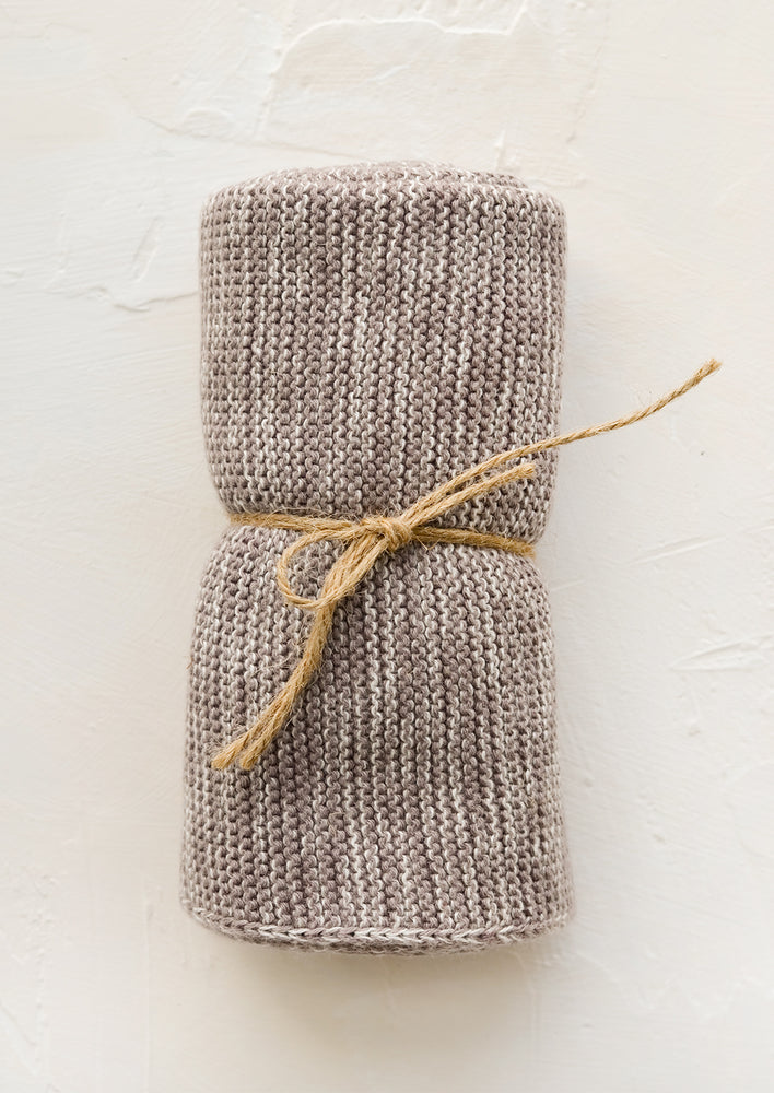 A knit cotton dish towel in taupe, rolled and tied with twine.