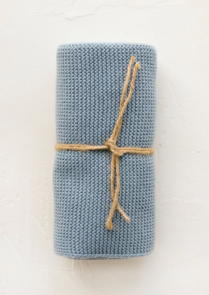 A knit cotton dish towel in wedgewood blue, rolled and tied with twine.