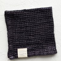 Charcoal: A folded waffle-weave linen washcloth in charcoal with a logo patch.