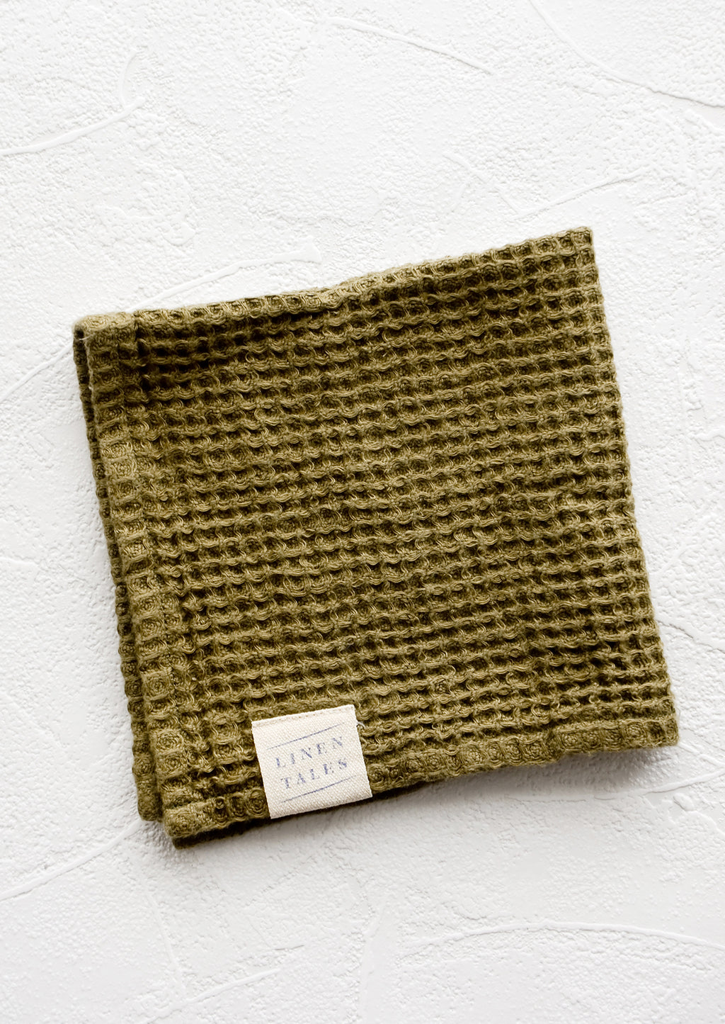Olive: A folded waffle-weave linen washcloth in olive green with a logo patch.