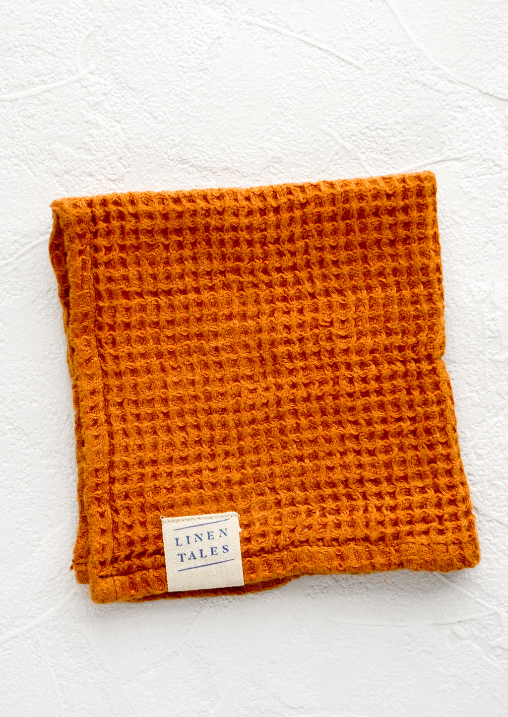 Terracotta: A folded waffle-weave linen washcloth in terracotta color with a logo patch.