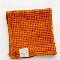 Terracotta: A folded waffle-weave linen washcloth in terracotta color with a logo patch.